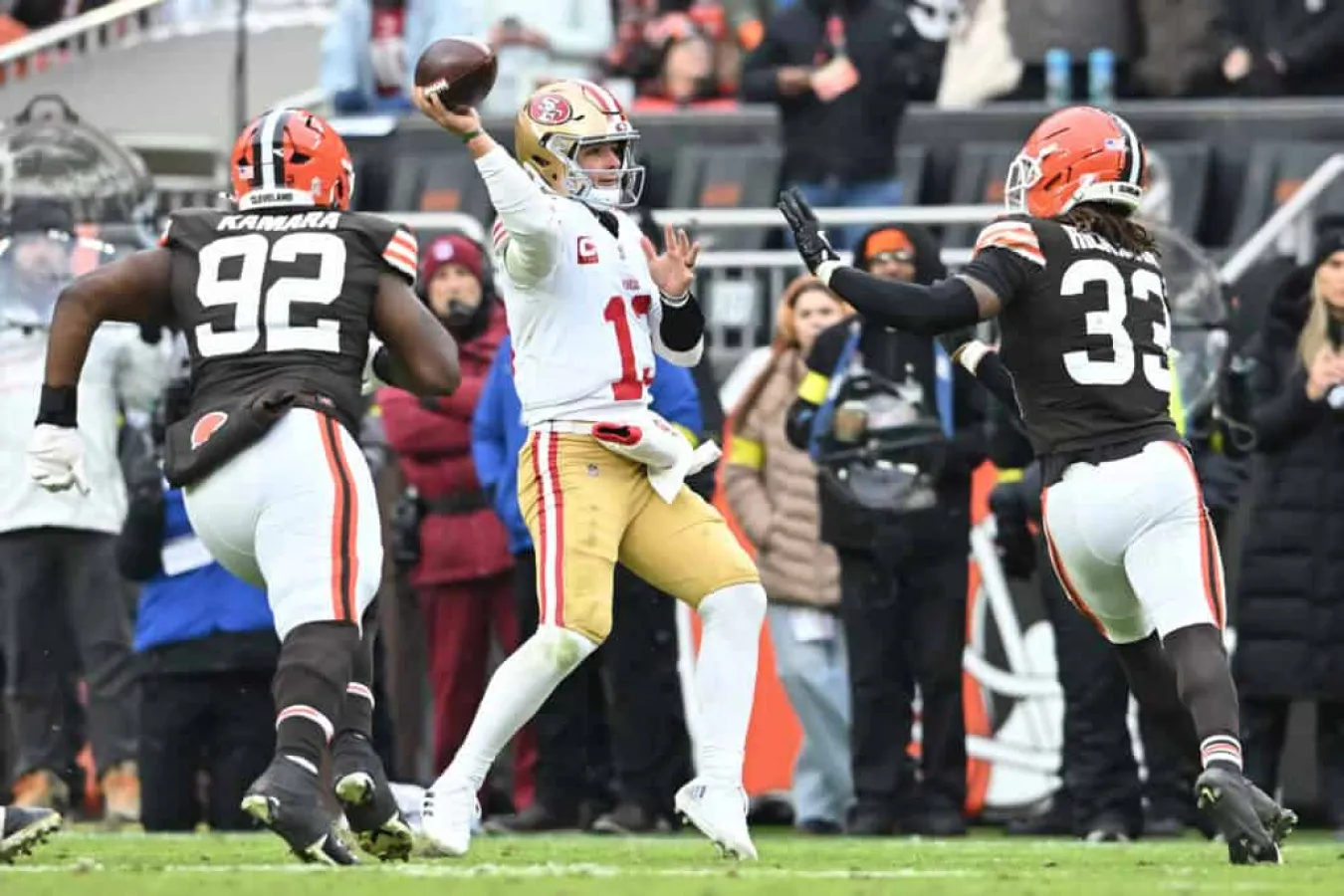 CLEVELAND, OHIO - NOVEMBER 30: Brock Purdy #13 of the San Francisco 49ers looks to pass while pressured by Sam Kamara #92 and Ronnie Hickman Jr. #33 of the Cleveland Browns in the third quarter of a game at Huntington Bank Field on November 30, 2025 in Cleveland, Ohio.