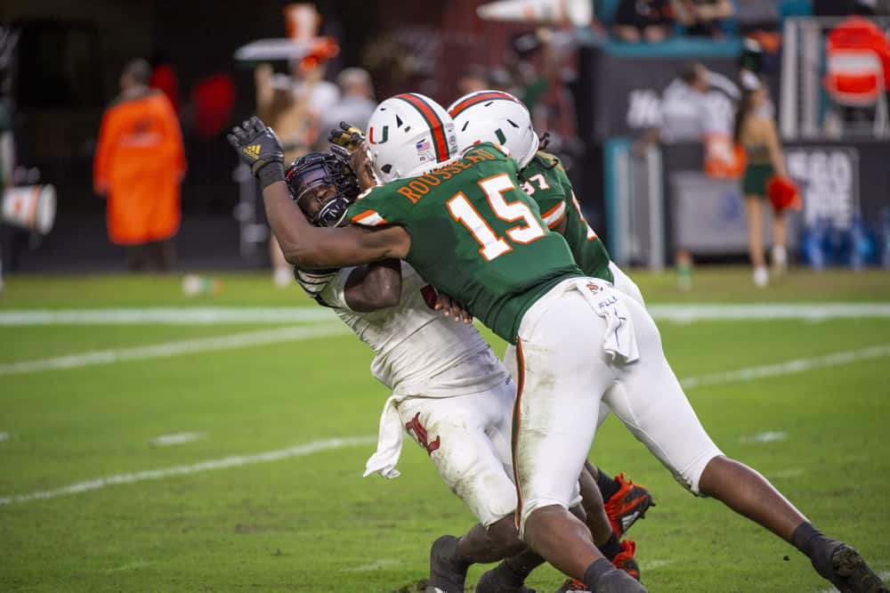 Louisville Cardinals quarterback Micale Cunningham (3) throws the ball and is tackled by Miami Hurricanes defensive lineman Gregory Rousseau (15) and Miami Hurricanes defensive lineman Jonathan Garvin (97) during the college football game between the Louisville Cardinals and the University of Miami Hurricanes on November 9, 2019 at the Hard Rock Stadium in Miami Gardens, Florida. 