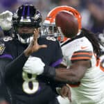 Quarterback Lamar Jackson #8 of the Baltimore Ravens pitches the ball while being hit by defensive end Jadeveon Clowney #90 of the Cleveland Browns at M&T Bank Stadium on November 28, 2021 in Baltimore, Maryland.