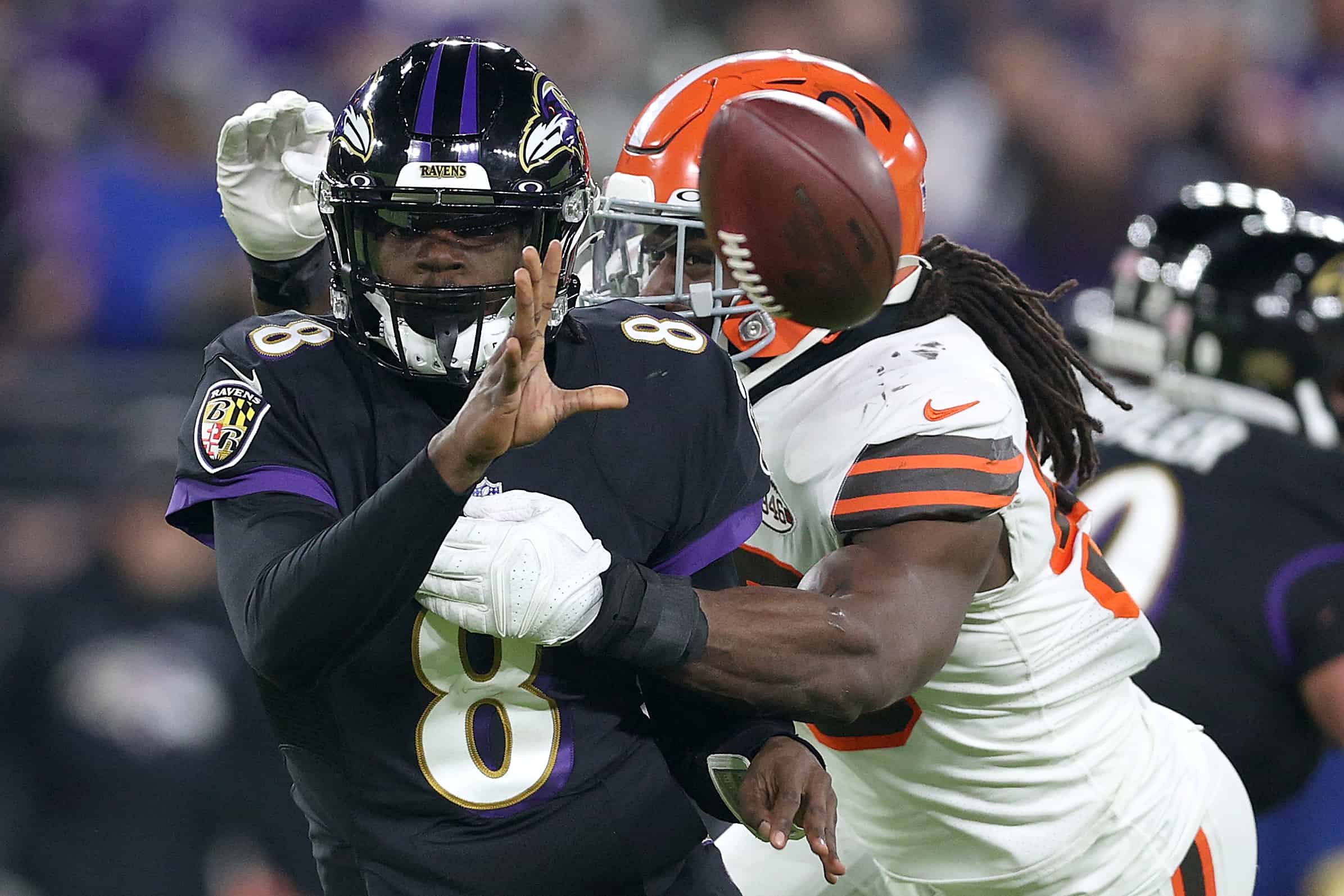 Quarterback Lamar Jackson #8 of the Baltimore Ravens pitches the ball while being hit by defensive end Jadeveon Clowney #90 of the Cleveland Browns at M&T Bank Stadium on November 28, 2021 in Baltimore, Maryland.