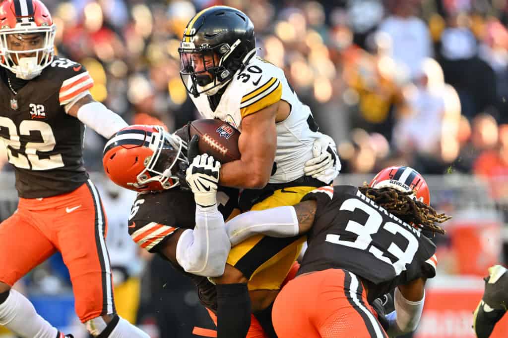 Jaylen Warren #30 of the Pittsburgh Steelers runs with the ball while being tackled by Jeremiah Owusu-Koramoah #6 and Ronnie Hickman #33 of the Cleveland Browns in the third quarter at Cleveland Browns Stadium on November 19, 2023 in Cleveland, Ohio.