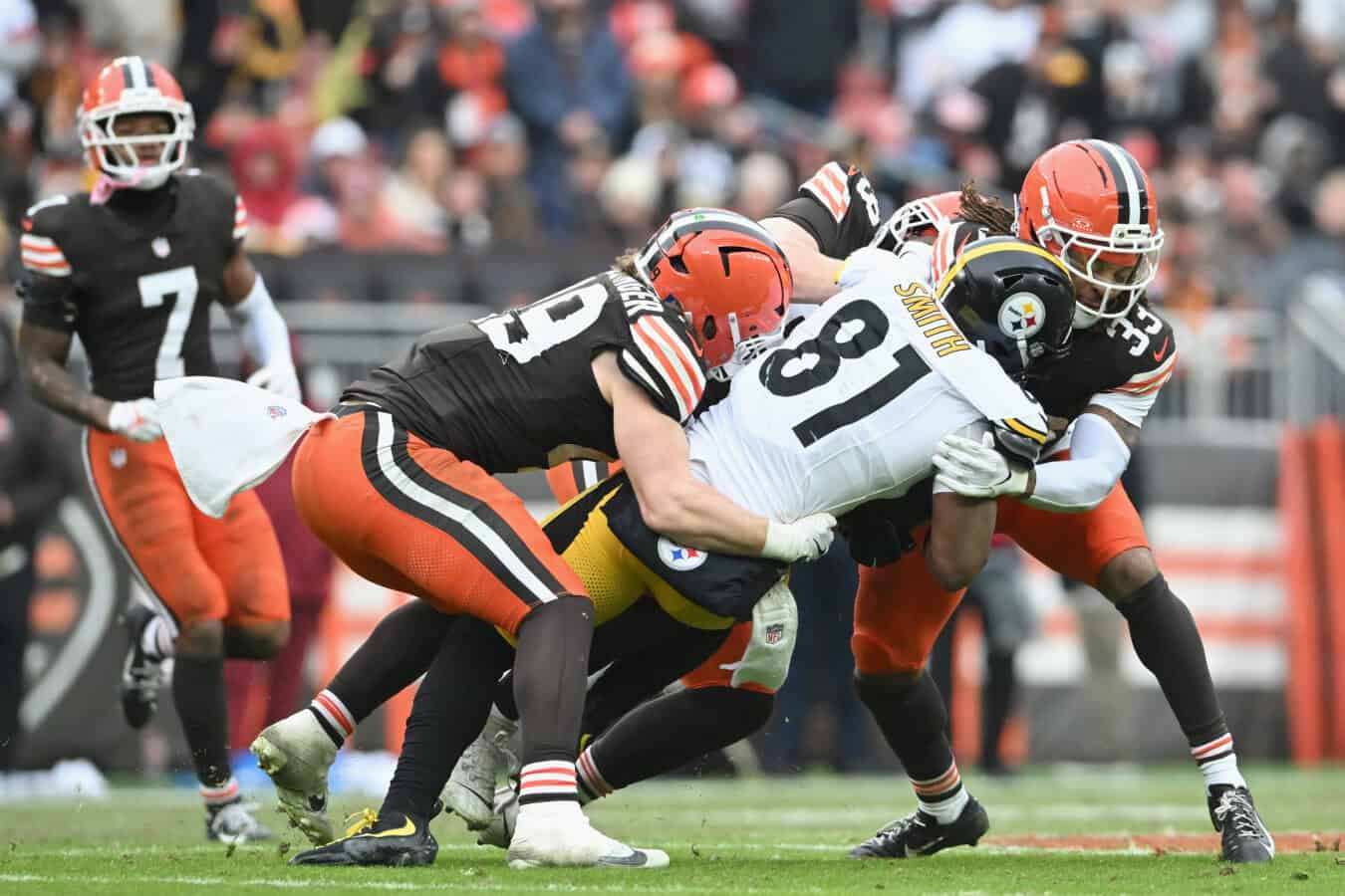 CLEVELAND, OHIO - DECEMBER 28: Jonnu Smith #81 of the Pittsburgh Steelers is tackled by Carson Schwesinger #49, Cameron Thomas #99 and Ronnie Hickman Jr. #33 of the Cleveland Browns during the third quarter at Huntington Bank Field on December 28, 2025 in Cleveland, Ohio.